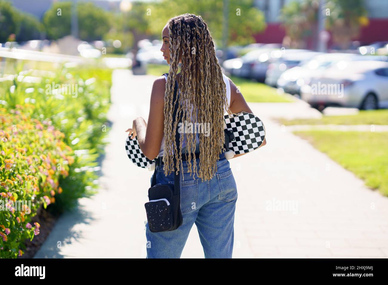 Black woman with colourful braided hairstyle, wearing a skateboard. Stock Photo