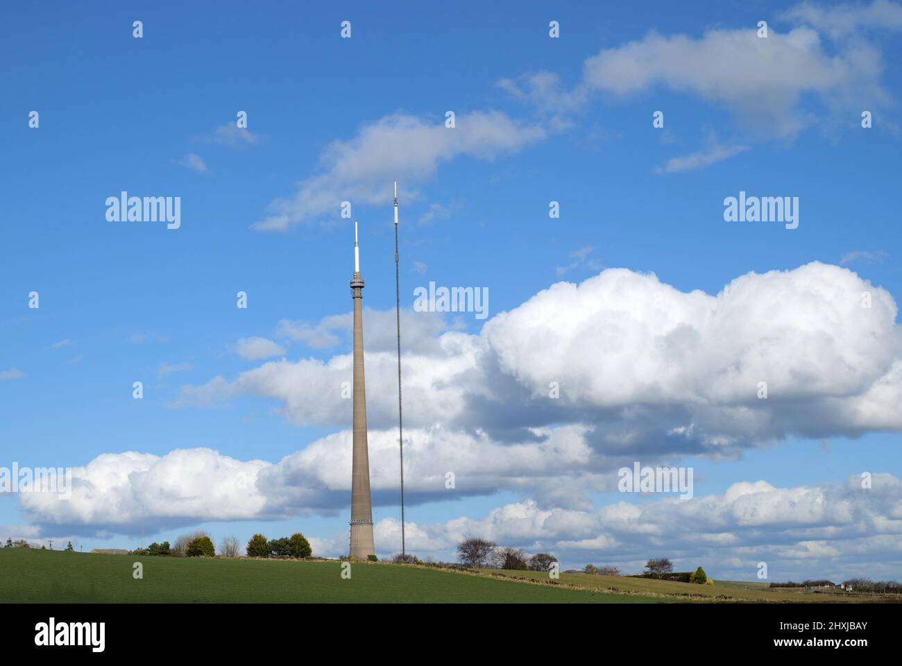 Two tall transmitter masts low white clouds in blue sky and green field Stock Photo