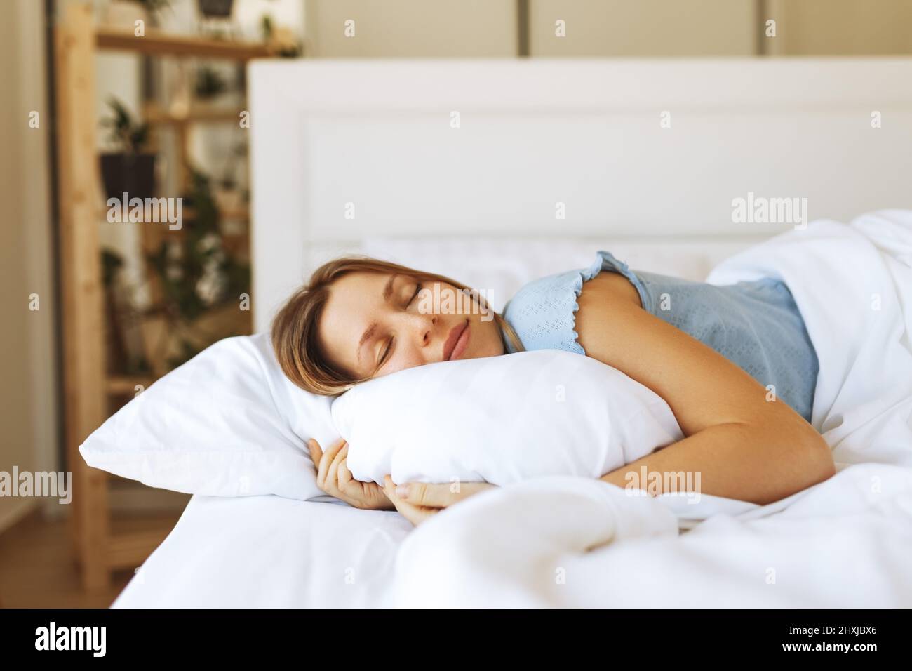 Portrait of young woman enjoying sleeping time in bed , close up ,elevated view, hugging pillow. Stock Photo