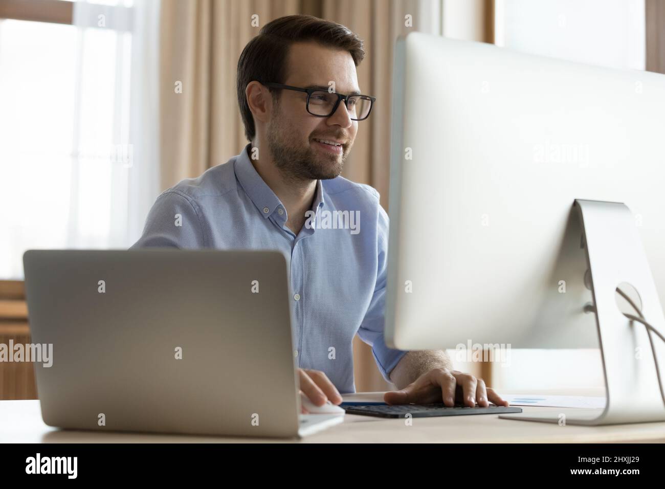 Smiling young man software developer using two computers in work Stock Photo