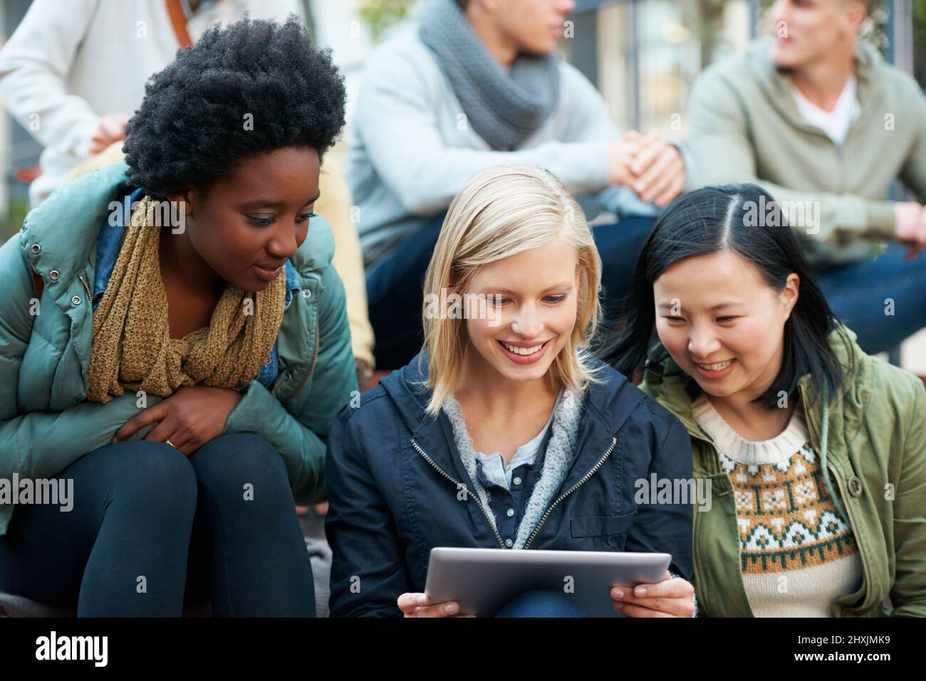 Look at this. Shot of a group of university students looking at something on a digital tablet. Stock Photo