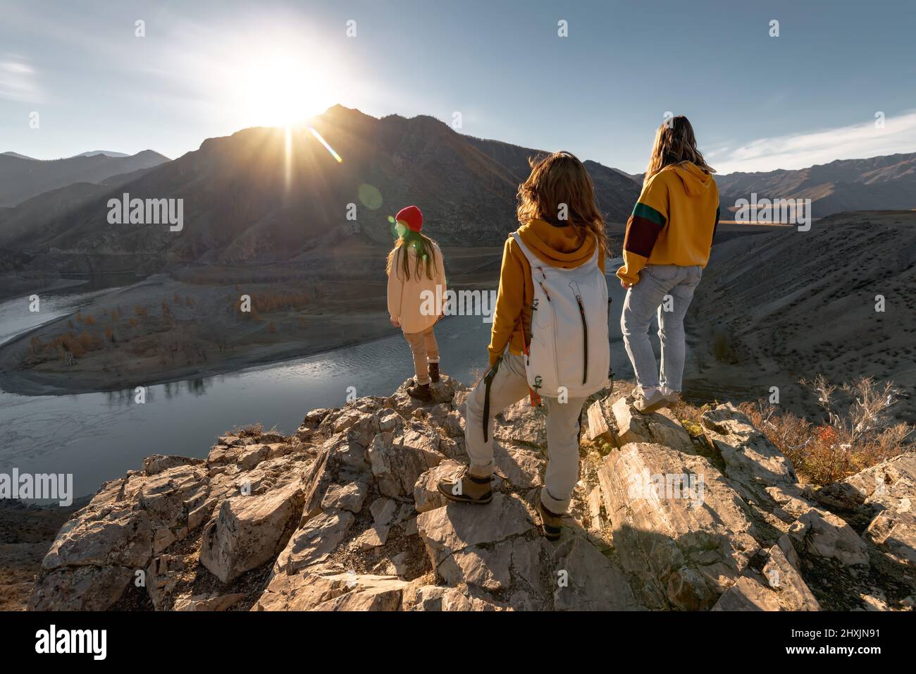 Group of three female hikers stands with backpacks at sunset view point Stock Photo