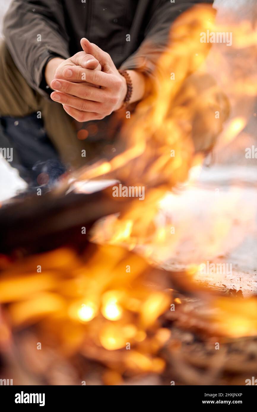 Man warming hands on bonfire in nature in cold season, winter. travel lifestyle photo. adventure active vacations outdoor. Extreme camping. in snowy f Stock Photo