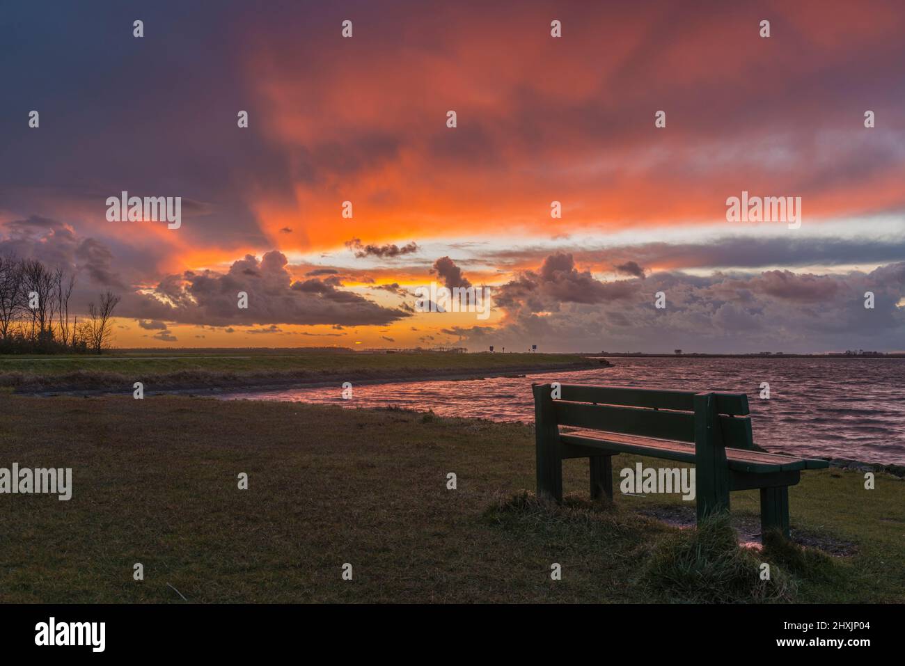 Dramatic thunderstorm clouds approaching a bench on the Veerse Meer at sunset. Zeeland, Netherlands Stock Photo