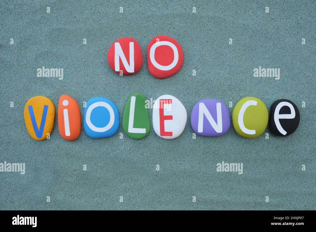 No violence, creative social slogan composed with hand painted multi colored stone letters over green sand Stock Photo