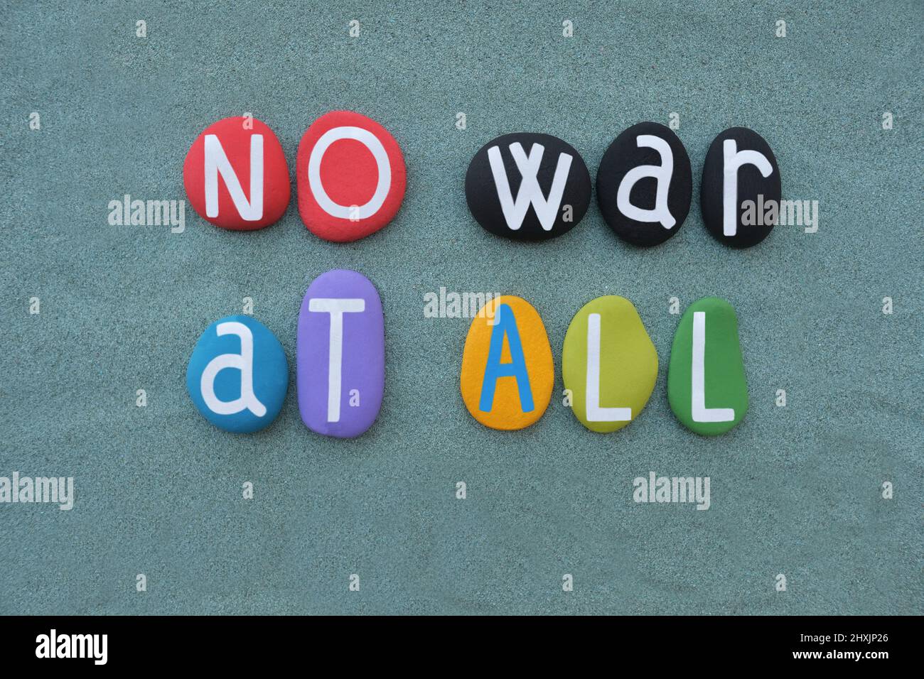 No war at all, creative slogan composed with hand panted multi colored stone letters over green sand Stock Photo