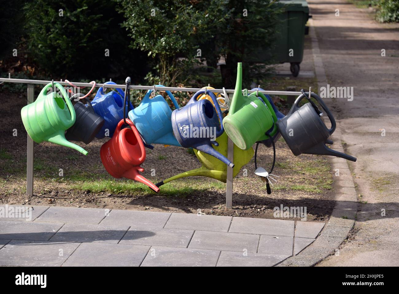 12 March 2022, North Rhine-Westphalia, Cologne: Colorful plastic watering cans hang on a stand at Melaten Cemetery and can be borrowed. Photo: Horst Galuschka/dpa Stock Photo