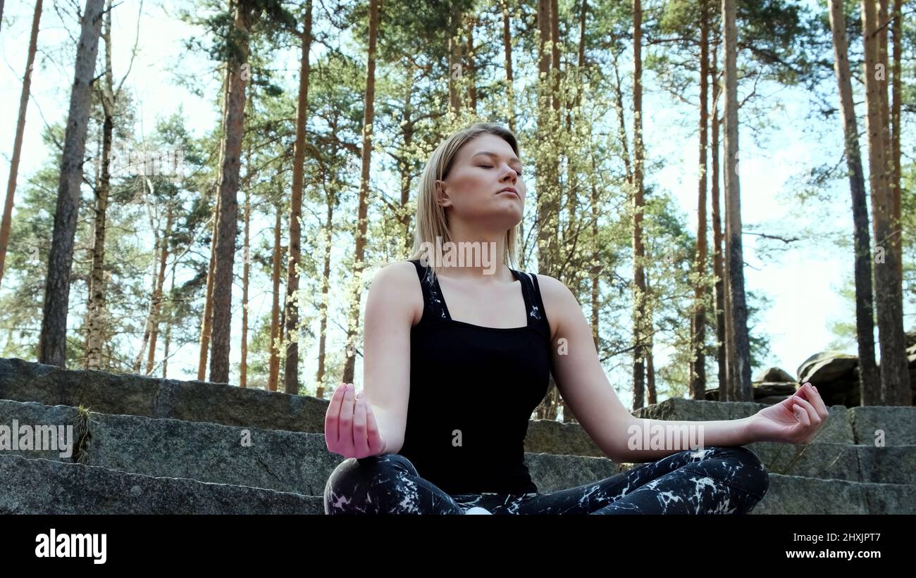 Happy woman deeply connected with nature feels unity and meditating in forest outdoors. Concept. Blond girl in sports suit sitting on concrete stairs Stock Photo