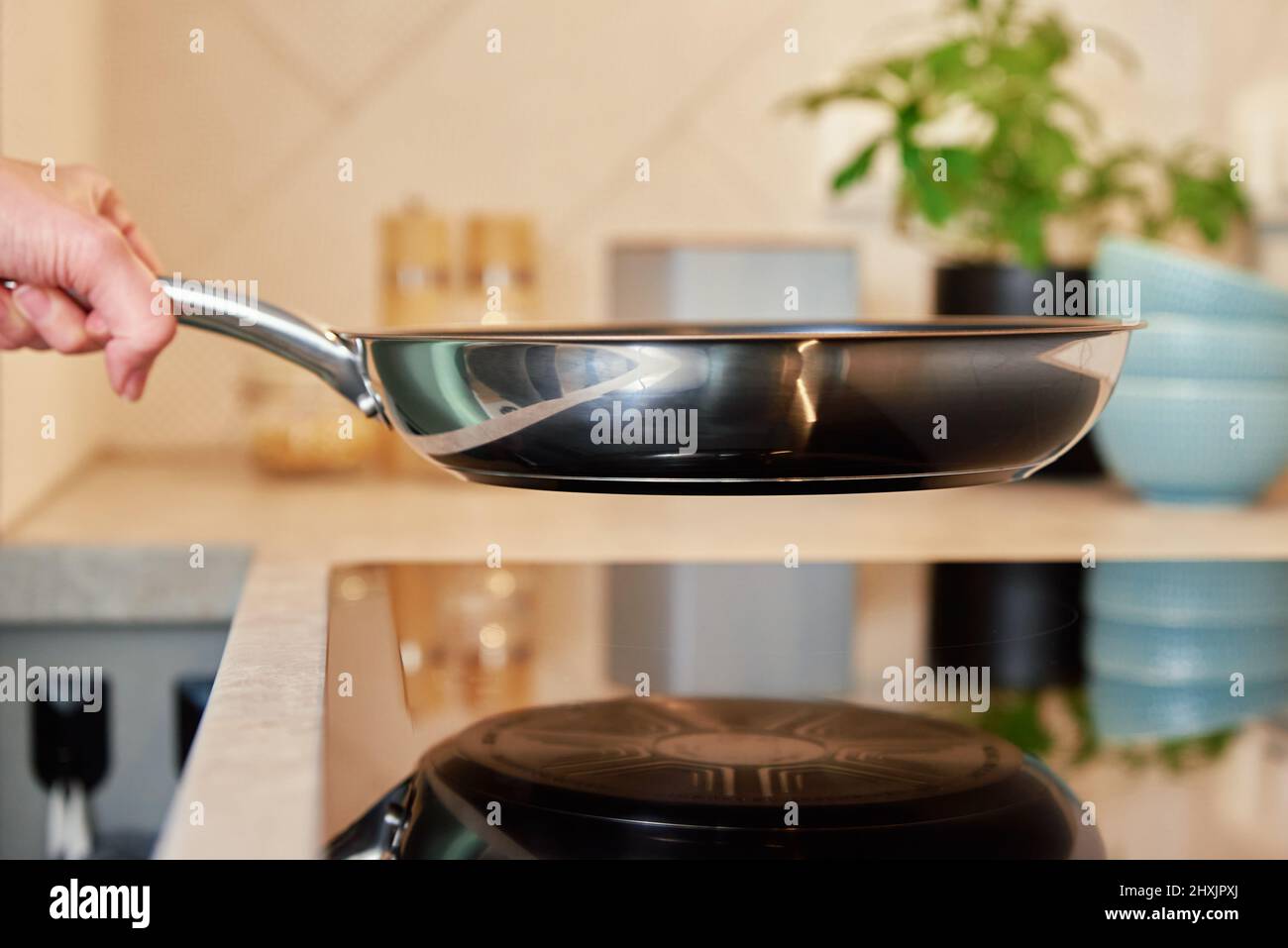 Woman hold steel frying pan on induction stove in the kitchen, Modern