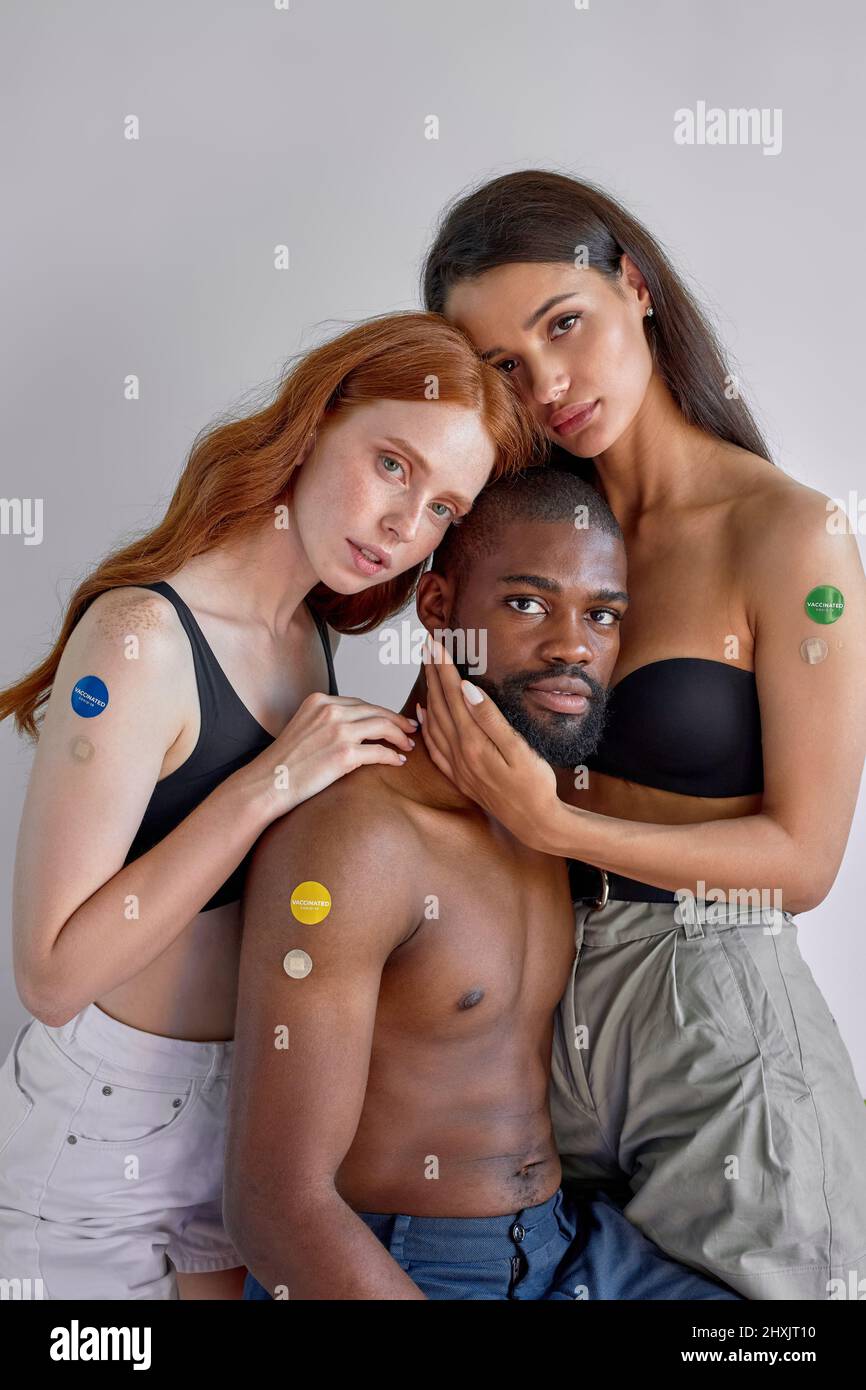 black guy and european women showing COVID-19 vaccine on arms, standing close to each other, posing. concept of coronavirus vaccination program to vac Stock Photo