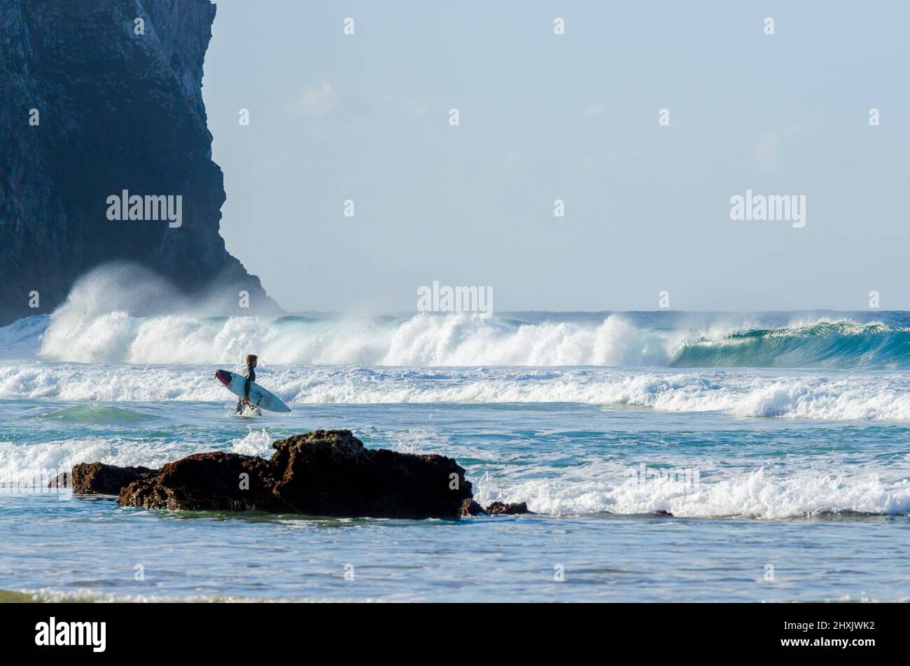 Surfer with board entering the waves at Praia de Castelejo, Vila de Bispo, Algarve, Portugal Stock Photo