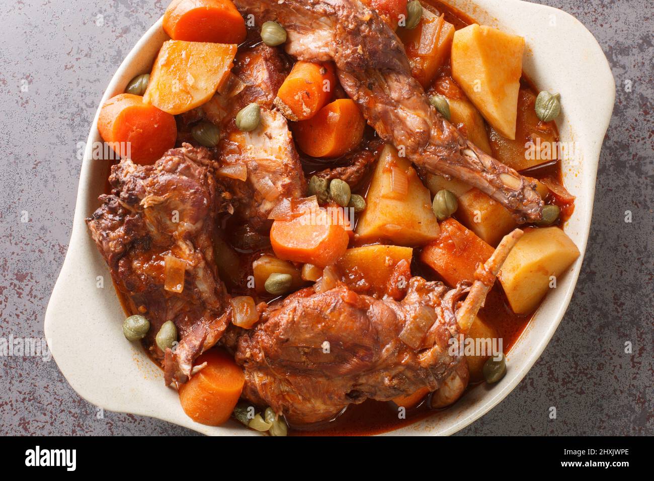 Rabbit stewed in red wine with vegetables and garlic close-up in a saucepan on the table. horizontal top view from above Stock Photo
