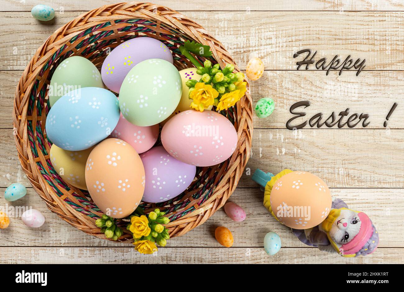 Colored easter eggs in a basket on a rustic wooden table.  Overhead view with Happy Easter text Stock Photo