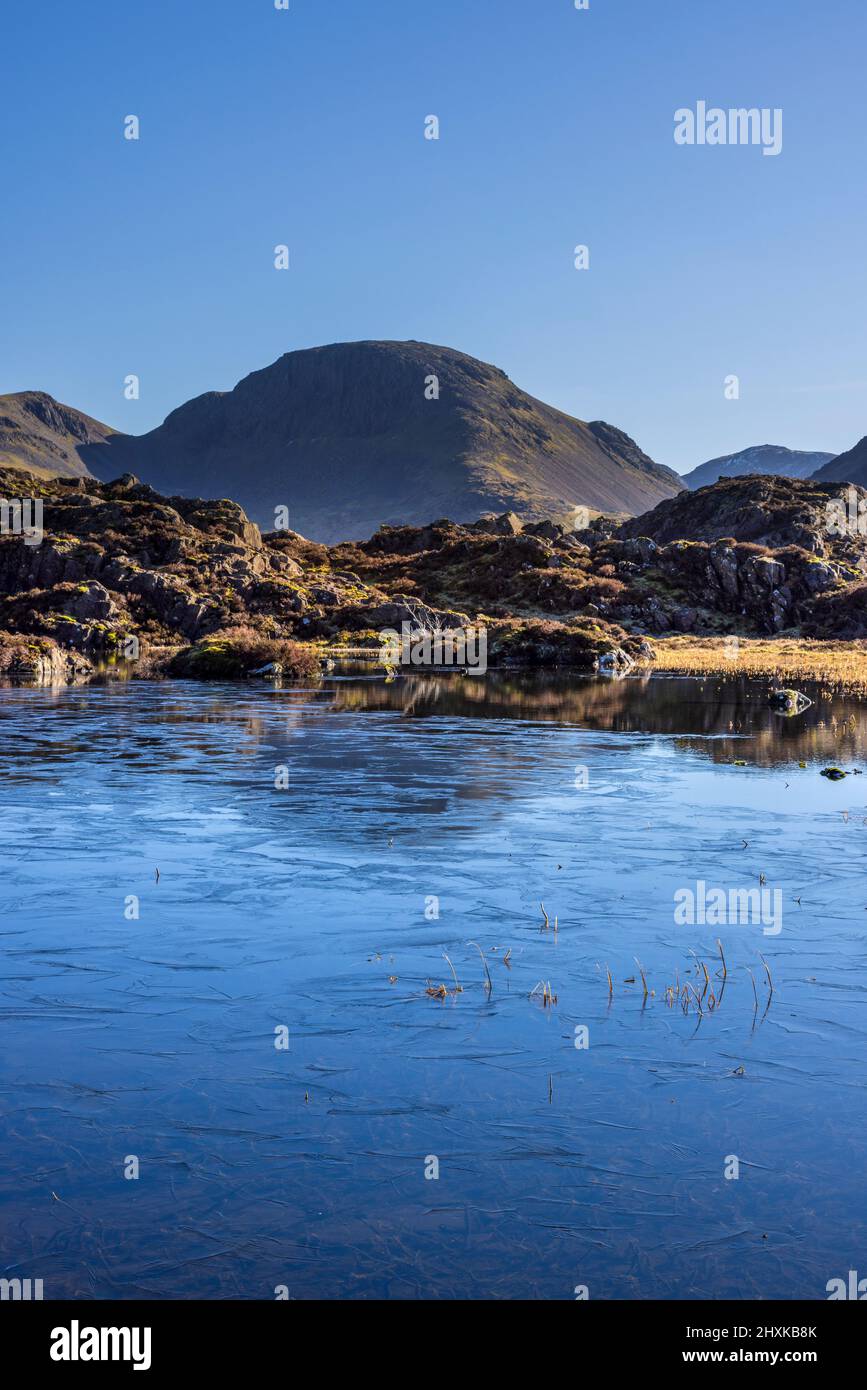 A frozen Innominate Tarn with Great Gable and Scar Fell Pike in the background, Lake District, England Stock Photo