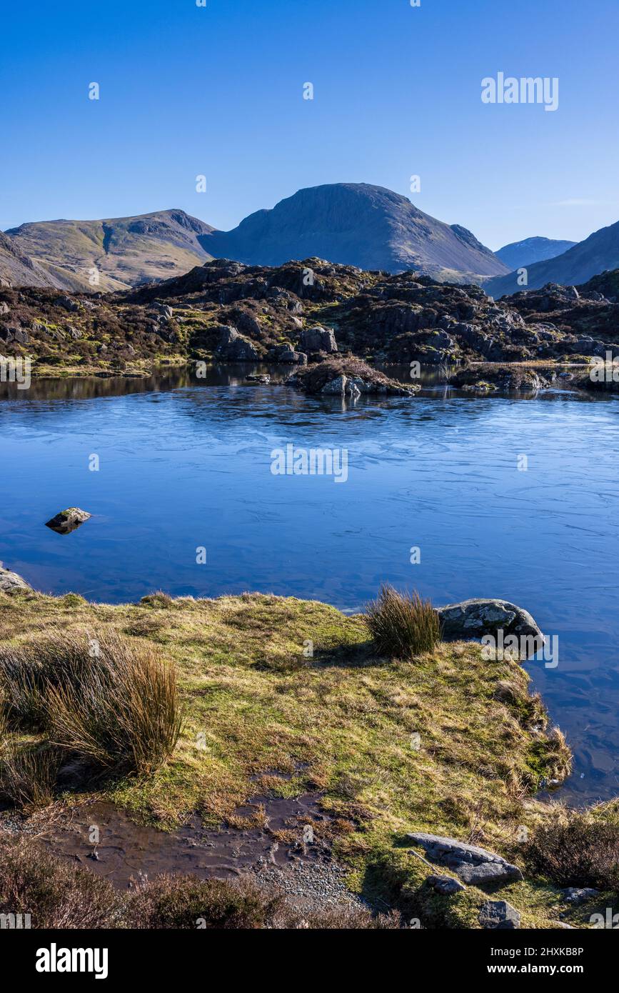 A frozen Innominate Tarn with Great Gable and Scar Fell Pike in the background, Lake District, England Stock Photo