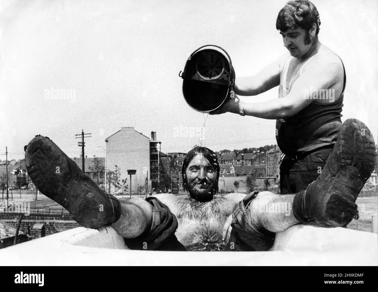 Shifting tons of scrap metal is no joke when the temperature is hitting the 80s. But it became a real pleasure when bearded Donald Morrison, 19, and 26 year old Frank Kay found a rusty old bath at J and W Robinson's yard in Partick, Glasgow. July 1976. Stock Photo