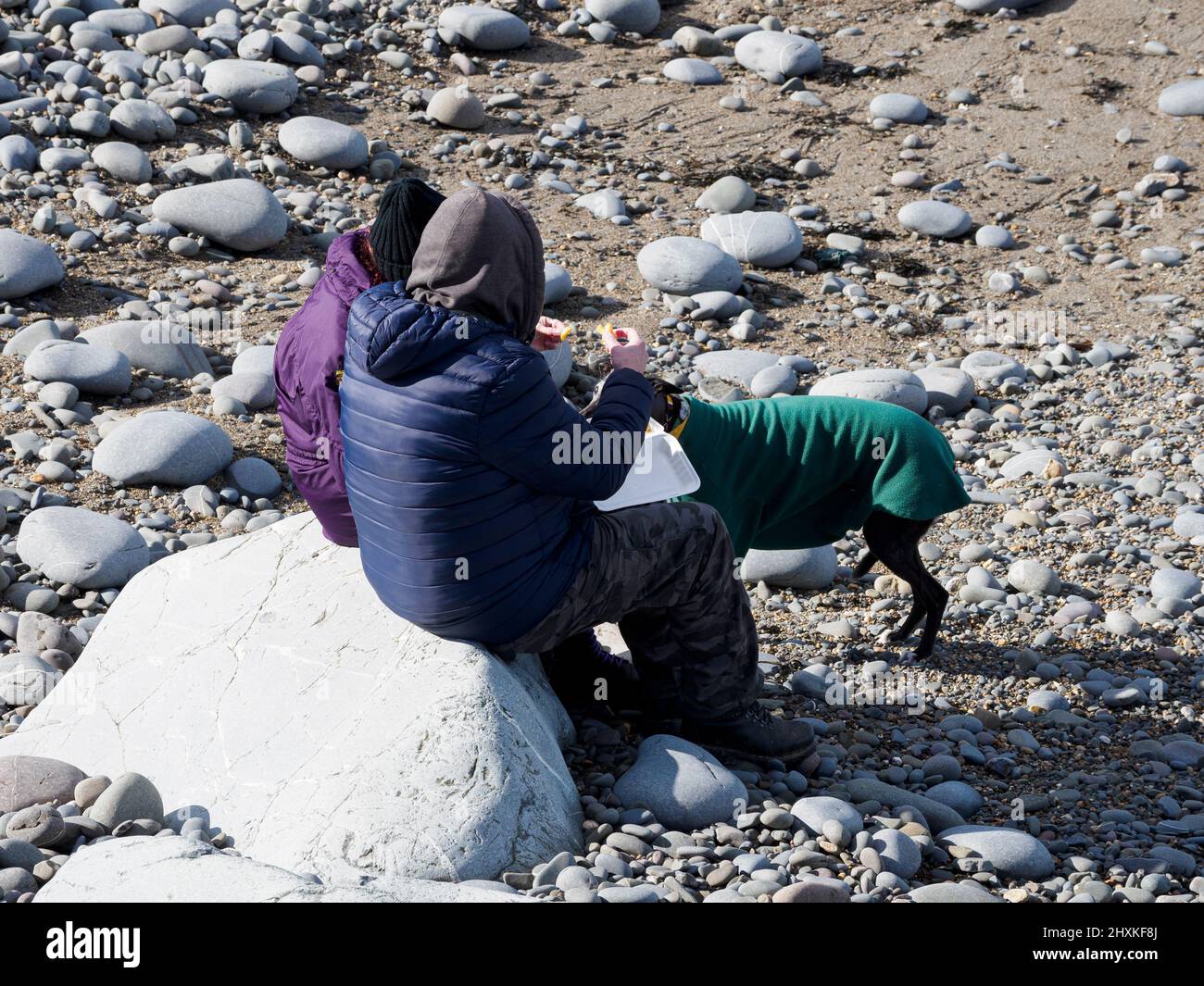 Couple sat on the beach eating chips on a cold spring day, Westward Ho!, Devon, UK Stock Photo