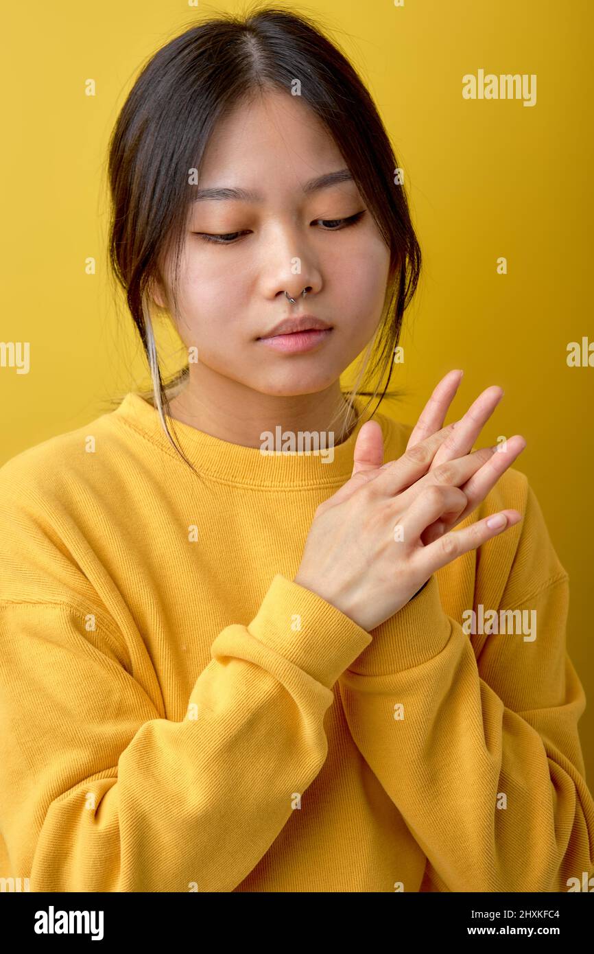 close-up portrait of chinese asian brunette female keeping hands together looking down thinking. attractive lady stand in contemplation, calm and paci Stock Photo