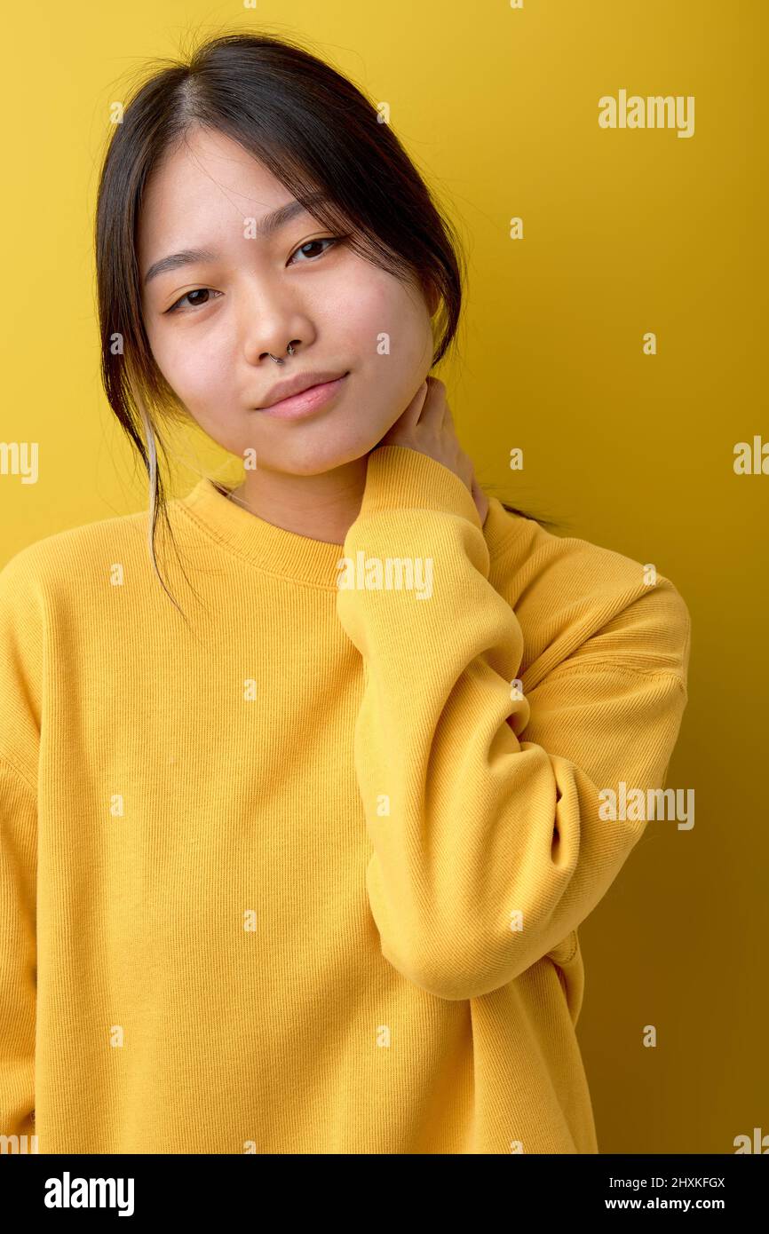 Cute Asian Female In Casual Outfit Looking Posing At Camera, Shy And Calm, Posing Isolated Over Yellow Studio Background, Close-up Portrait. Beautiful Stock Photo