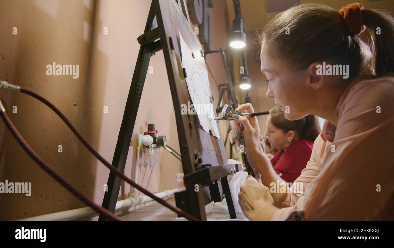 Woman artist learns to paint with airbrush with acrylic dye, paper and