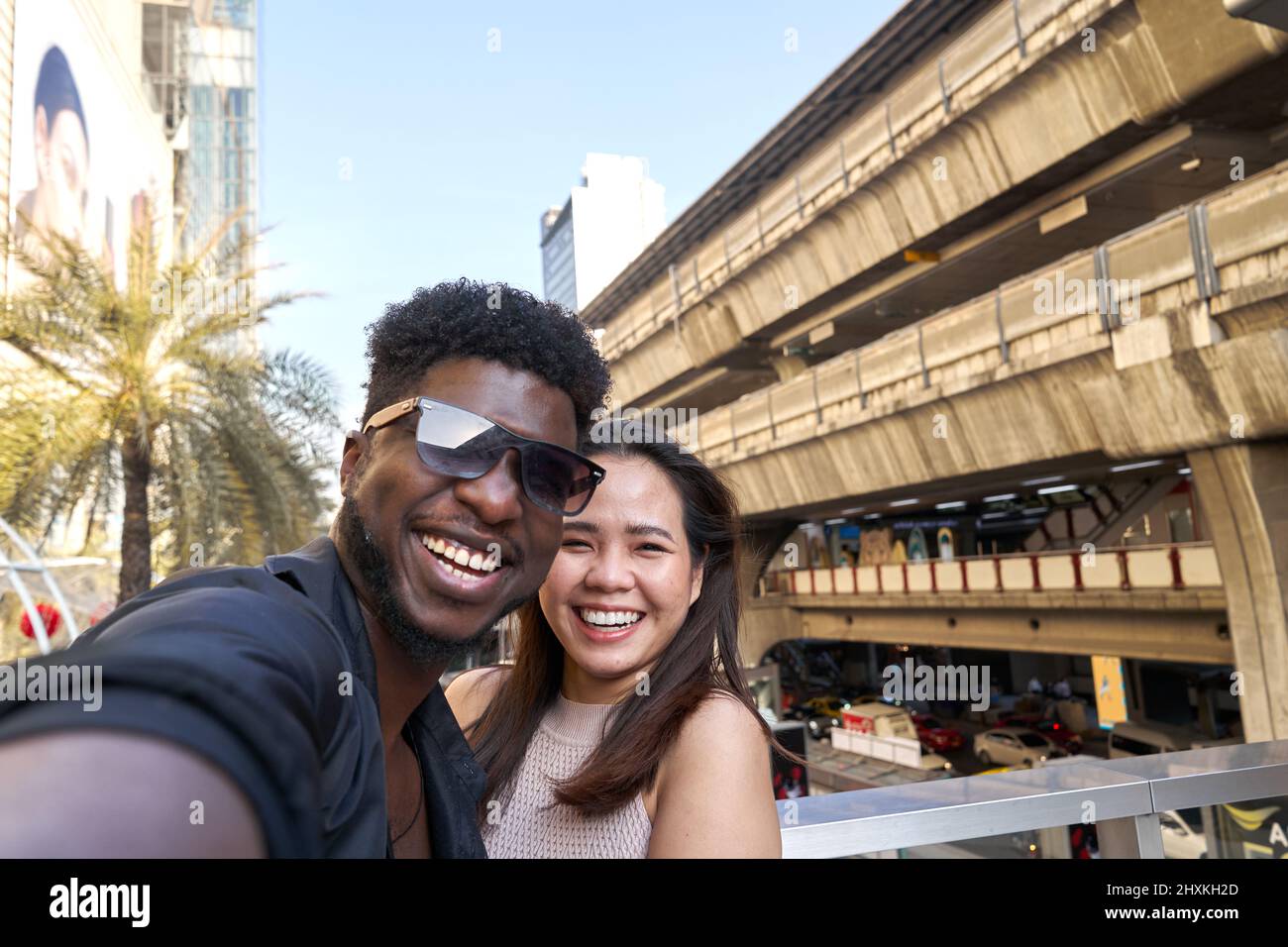 Two multethic smiling friends embracing while taking a selfie outdoors Stock Photo