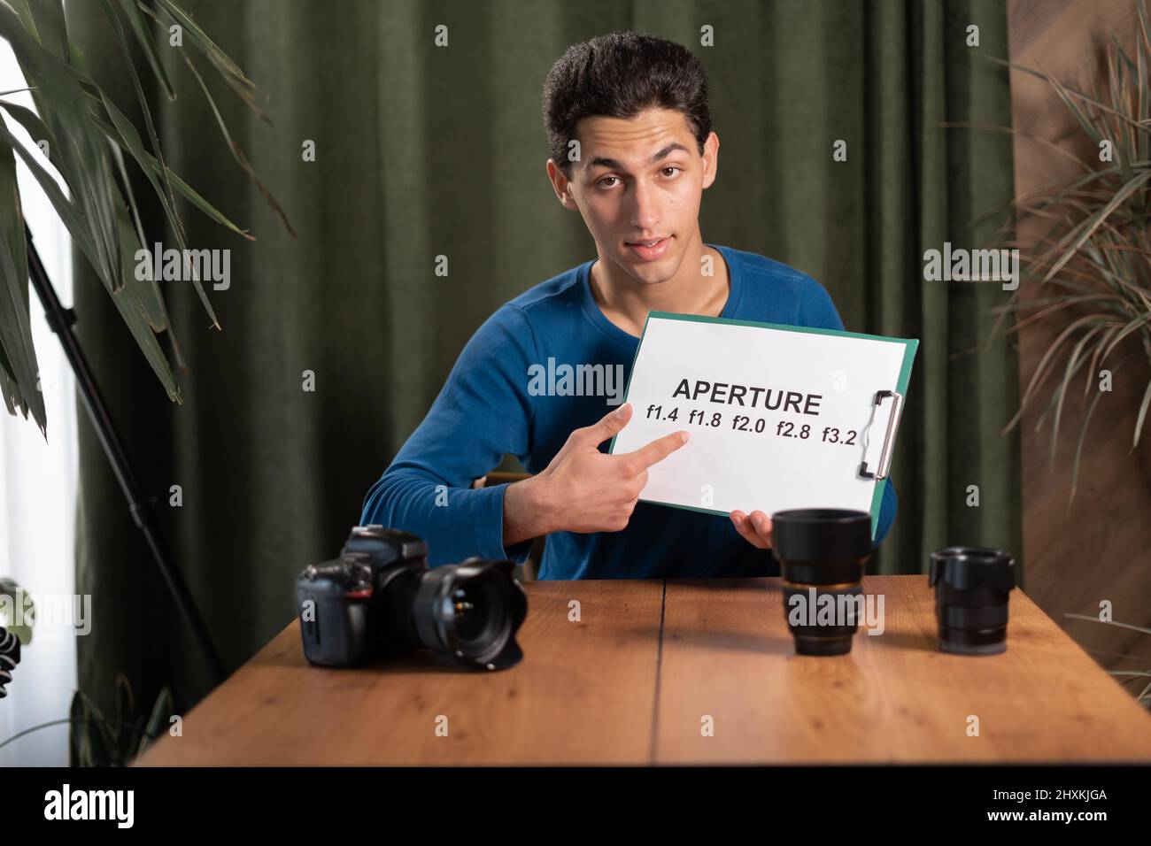 arab Guy-photographer is recording a video tutorial for photographers holding a plate with the aperture value in his hands. Online photography trainin Stock Photo