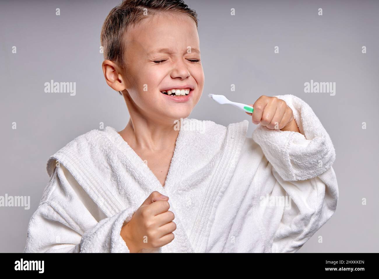 Portrait of little teen boy brushing teeth at morning. Child dental hygiene and healthcare. caucasina kid boy in white bathrobe cares of dental health Stock Photo