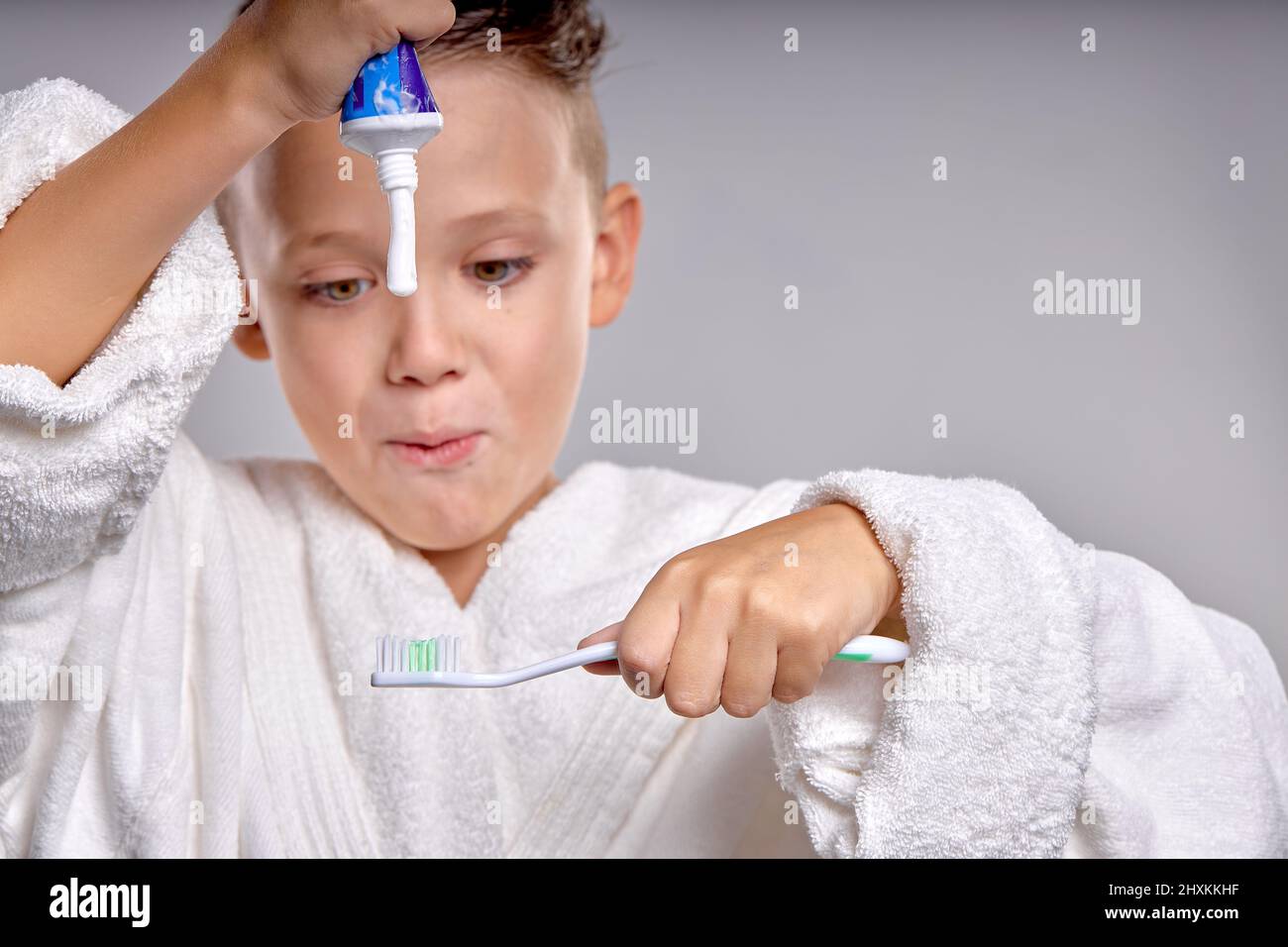 emotional Child going to brush teeth, applying paste on tooth brush, wearing bathrobe in the morning. Dental hygiene and health for children. isolated Stock Photo