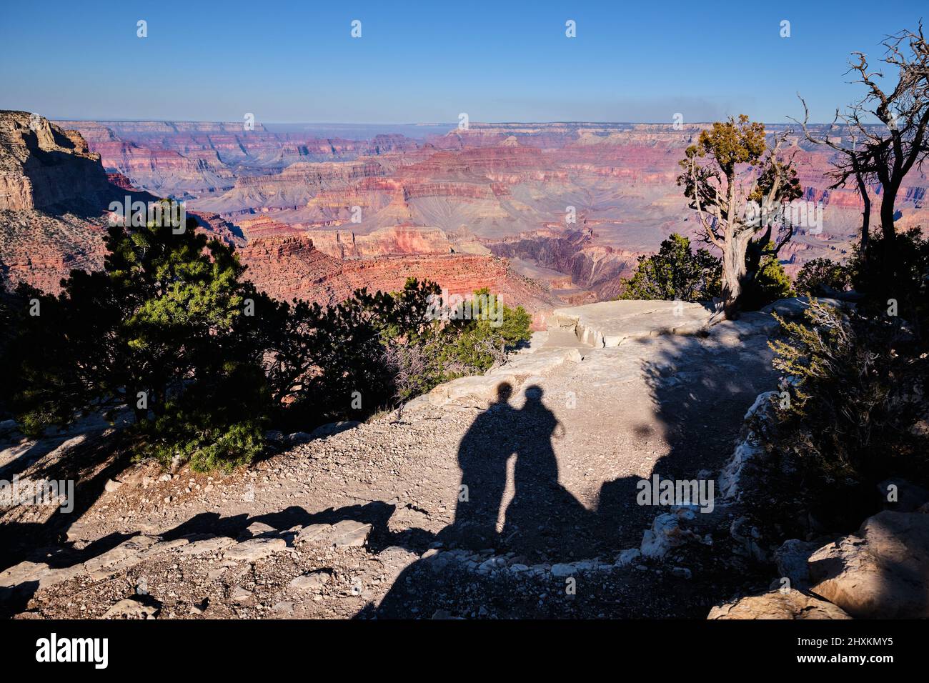 Shadows of two people touching at the shoulder on outcrop near Yavapai Point with a wide view of Grand Canyon spreading out in the background Stock Photo