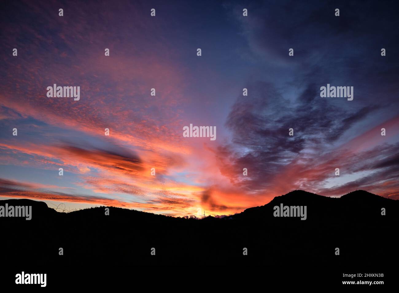Silhouette of rounded mountains below glorious sunset skies of pink, orange, red, mauve and yellow over Starr Pass, Tucson, Arizona Stock Photo
