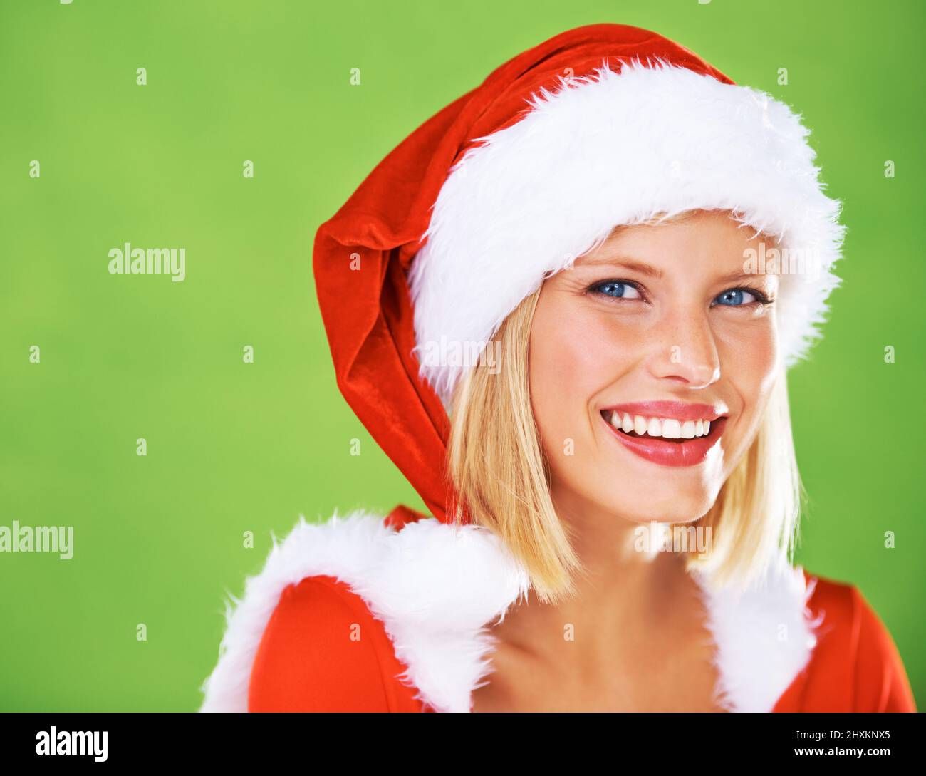Promoting your Christmas message. Cute portrait of a happy young female modeling a red Father Christmas hat with white fur trim, isolated on green - Stock Photo