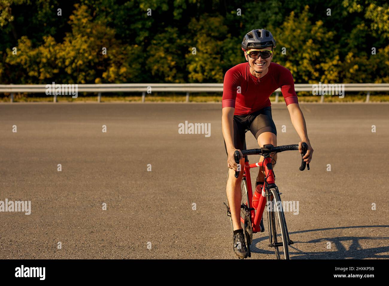 Cyclist in sportswear rides bicycle on road. Athlete Man is walking on a bicycle in nature. Sport concept. European caucasian male in red t-shirt, sho Stock Photo