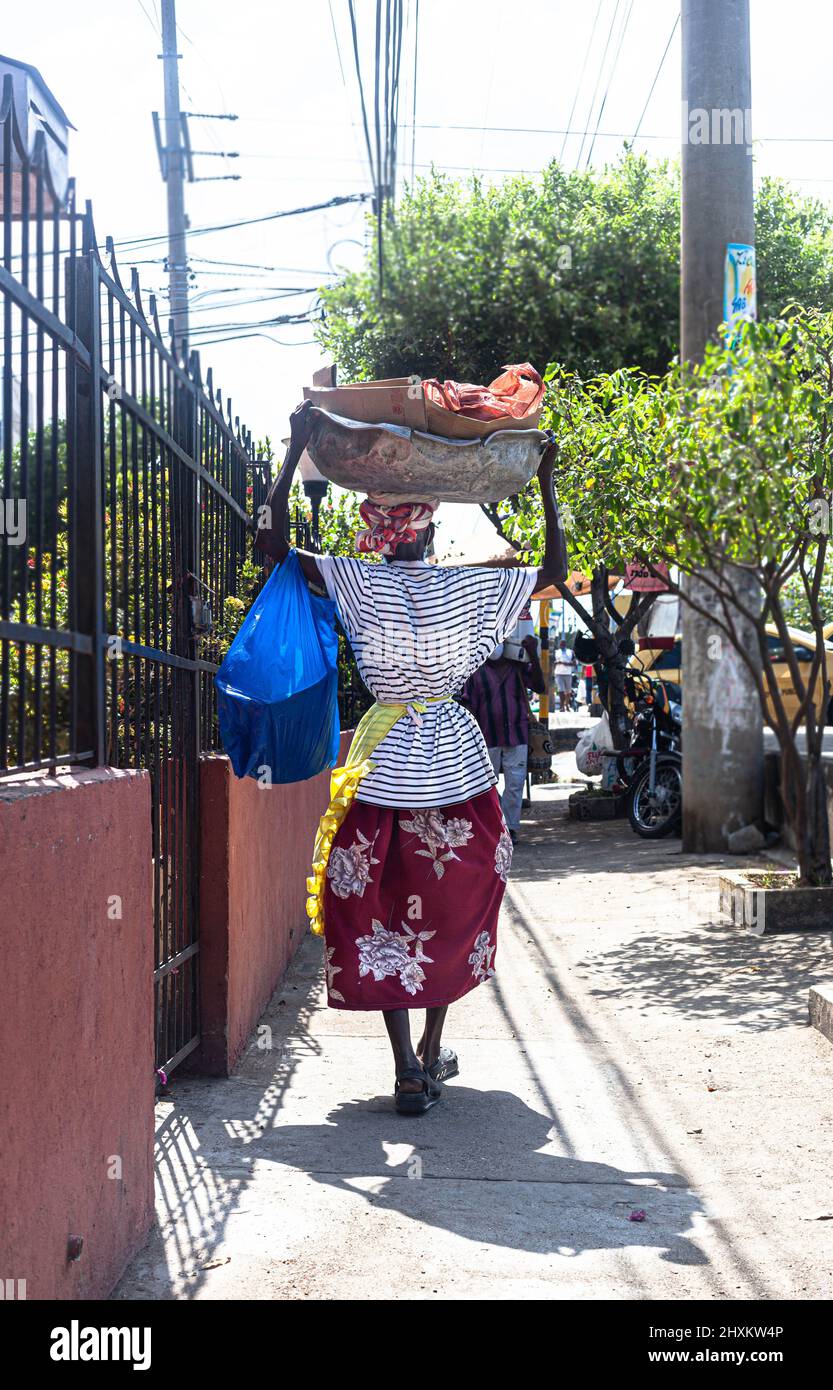 Full length portrait of a senior street vendor, palenquera, walking away, holding a large bowl on her head, Cartagena de Indias, Colombia. Stock Photo