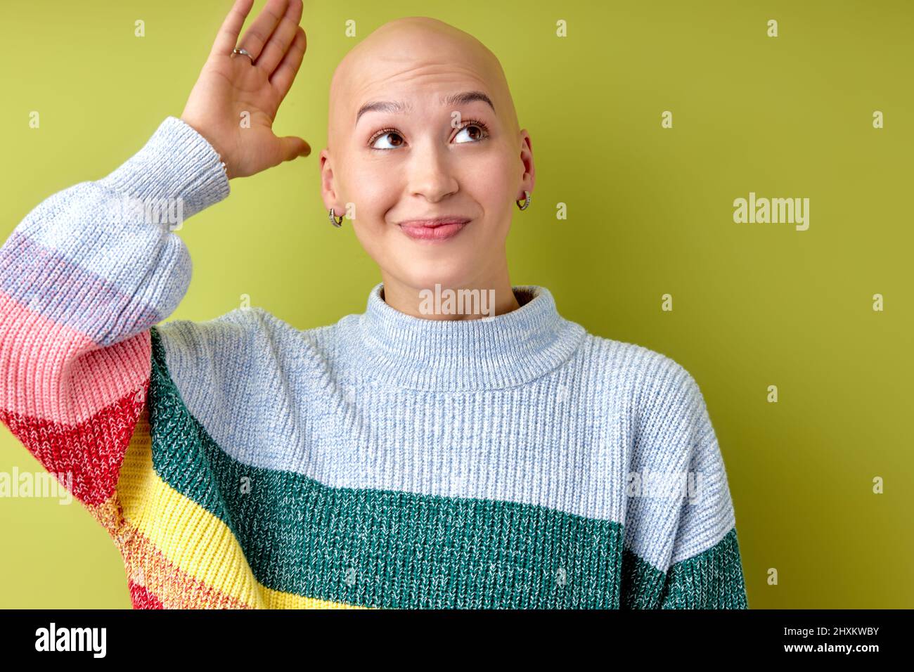 Portrait of positive excited bald female looking up with funny surprised face isolated on green studio background. Young hairless woman posing at came Stock Photo