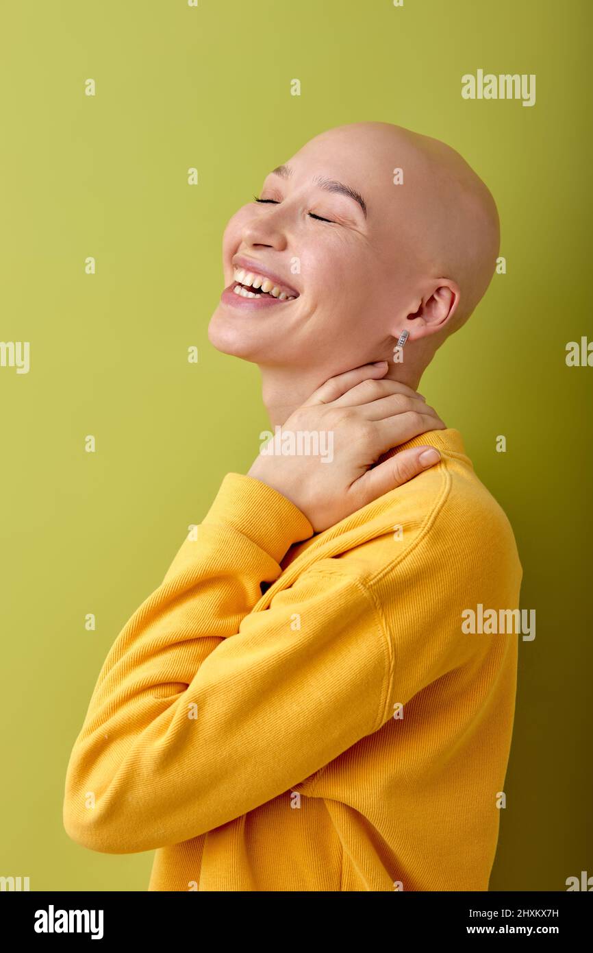 Laughing. young caucasian bald woman posing on green studio background. Human emotions, facial expression,sales, ad concept. Youth culture. Female wit Stock Photo