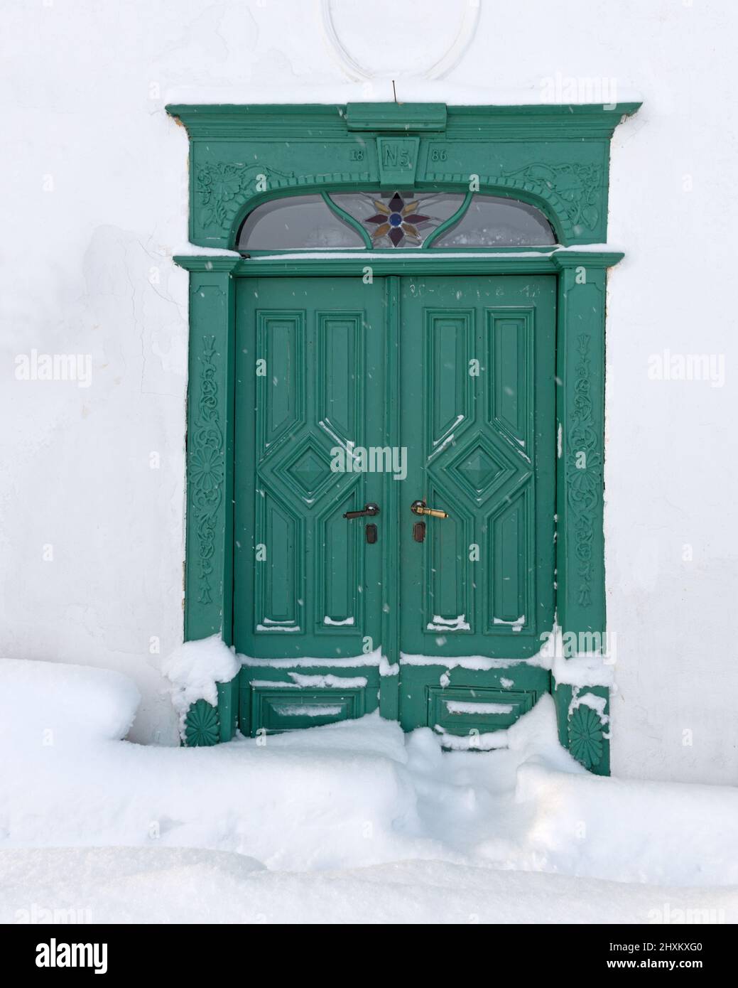 carved green old wooden door with deep fresh snow in front Stock Photo