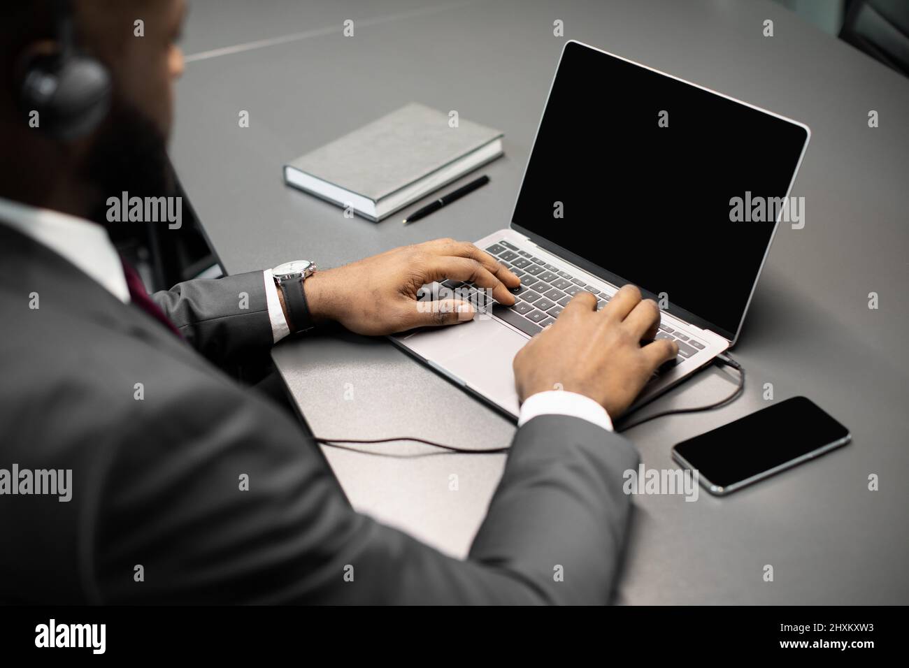 Unrecognizable black businessman using laptop with empty screen and headset Stock Photo