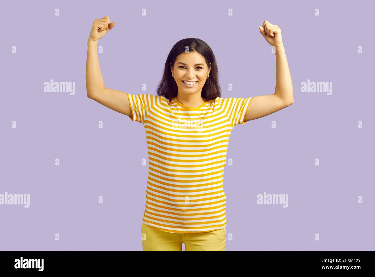 Cheerful funny woman demonstrates biceps muscles as sign of success and health on purple background. Stock Photo