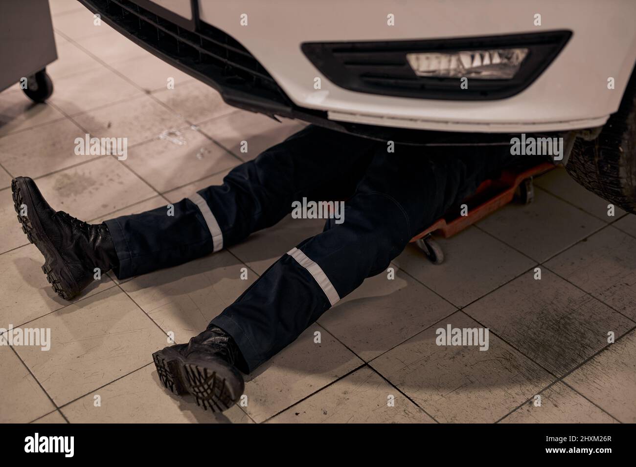 auto mechanic male working alone on floor repairing bottom of car, look at details, troubleshoot the car. cropped male car mechanic in uniform checkin Stock Photo
