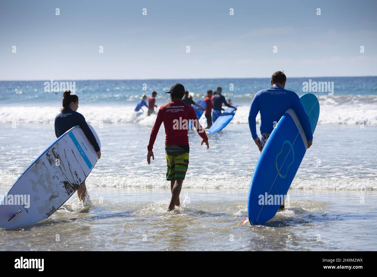A surf instructor takes his students into the Pacific Ocean for surf