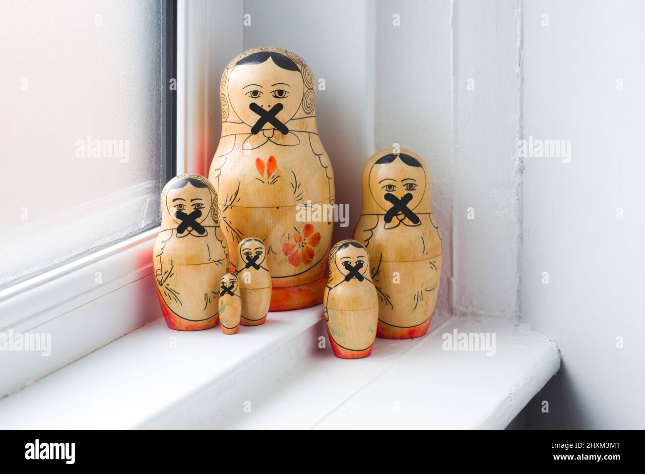 Family of Russian Dolls in a grouping on a window sill with their mouths crossed out so they cannot speak Stock Photo