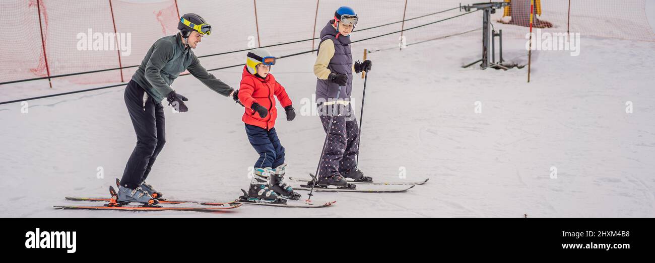 BANNER, LONG FORMAT Mom and son are learning to ski with an instructor. Active toddler kid with safety helmet, goggles and poles. Ski race for young Stock Photo