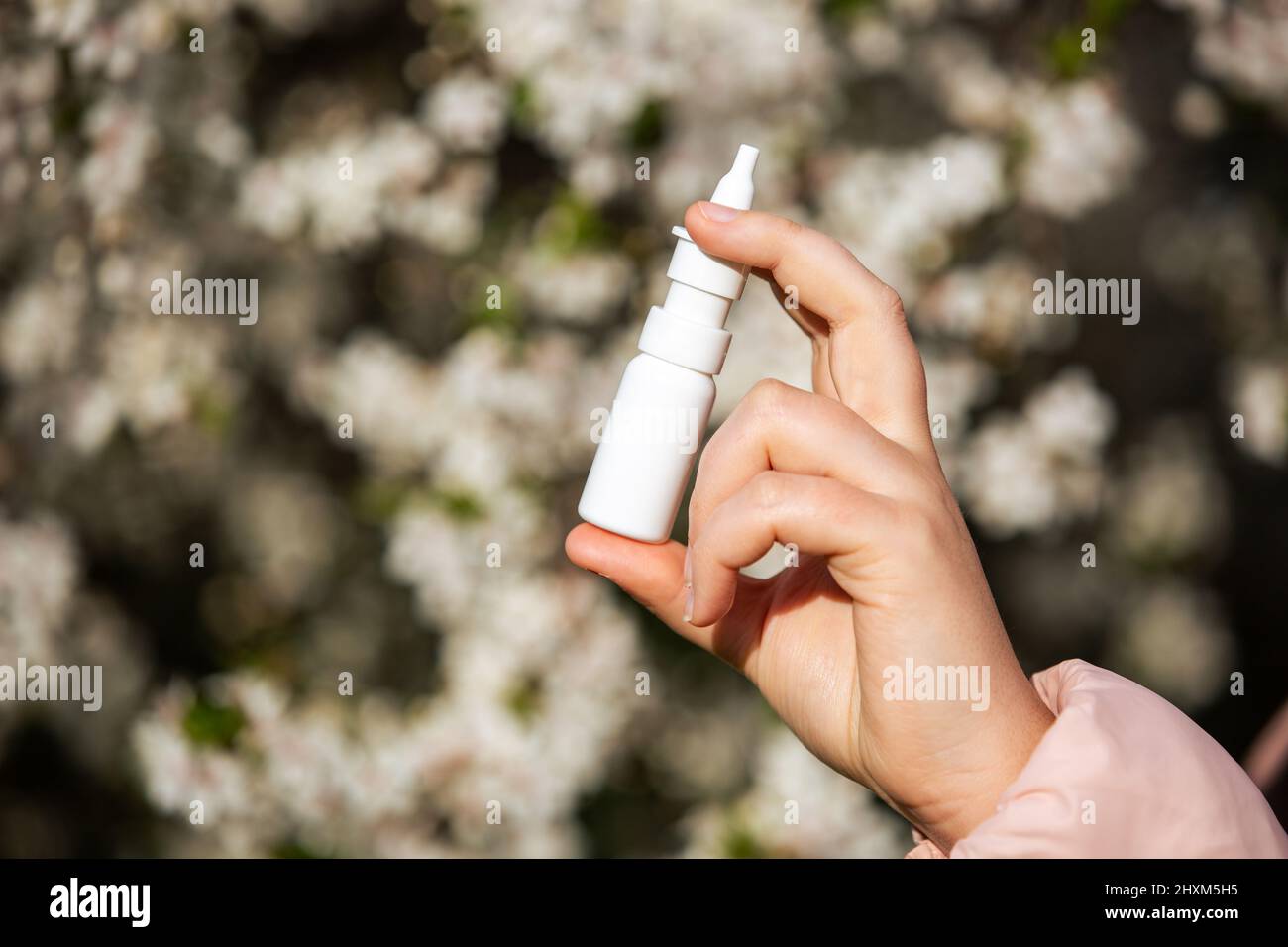 Allergy concept, young woman with nose or nasal spray in hand in front of blooming a tree during spring season, healthcare Stock Photo