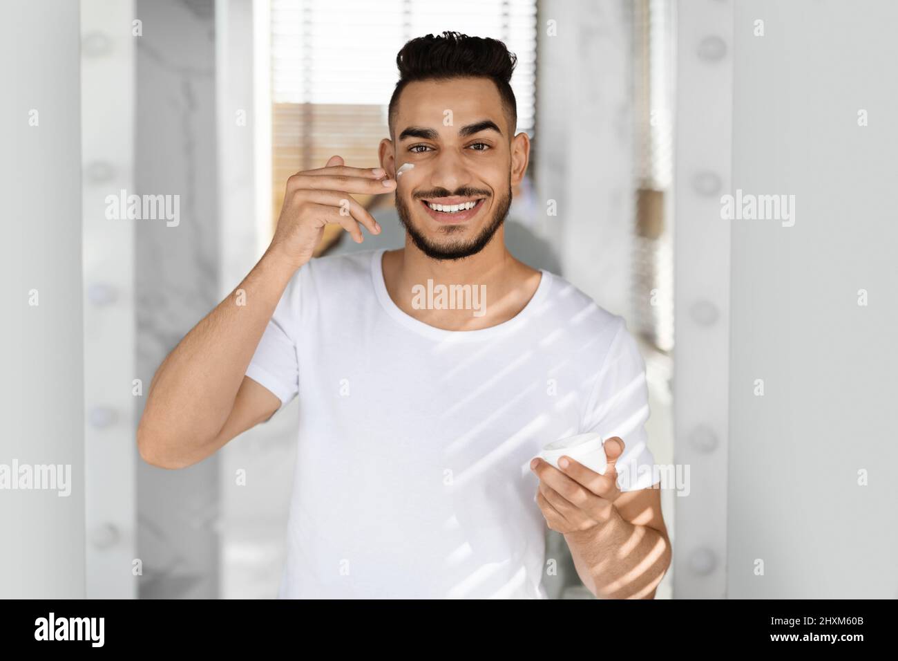 Skincare Concept. Attractive Middle Eastern Man Applying Moisturising Cream On Face Stock Photo