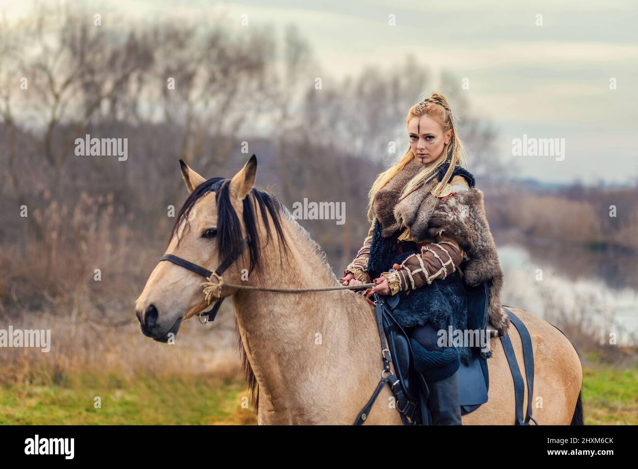 Portrait of beautiful viking woman warrior with painted face and braids riding horse in forest Stock Photo