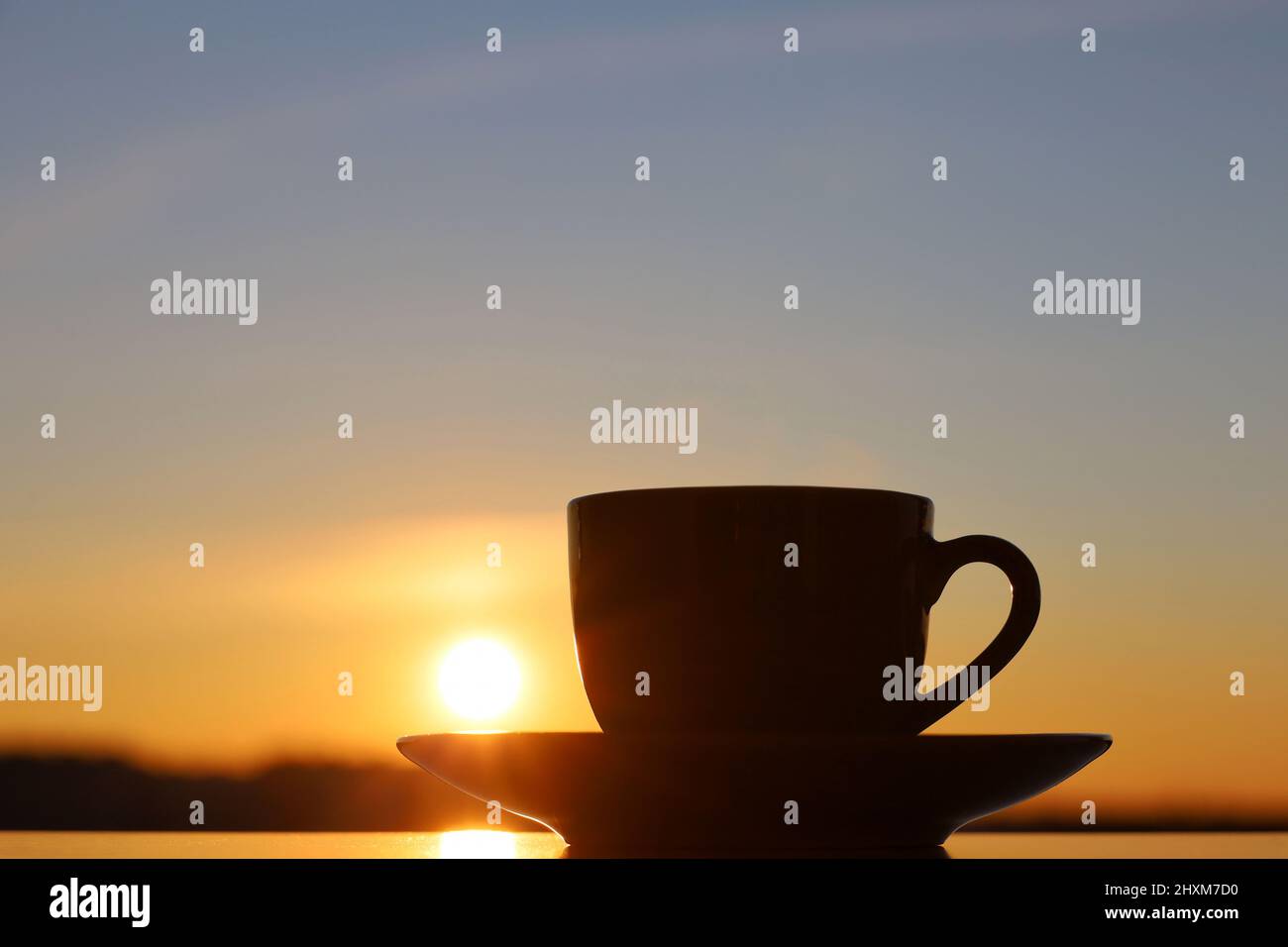 Silhouette of coffee or tea cup on background of sunset sky and shining sun. View from the window to evening city Stock Photo