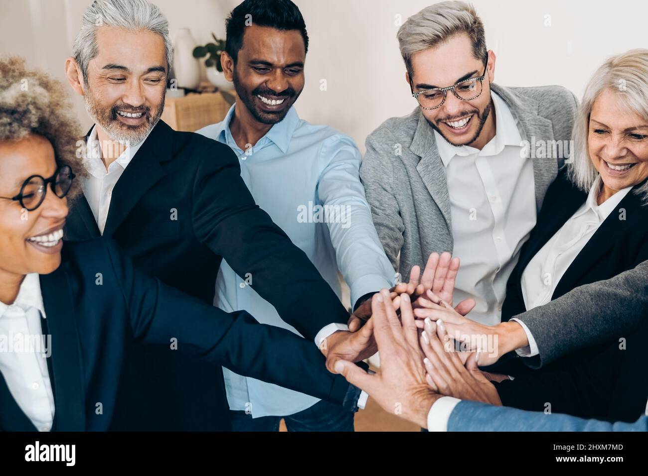 Multiracial business people celebrating together stacking hands inside modern office - Focus on asian man face Stock Photo