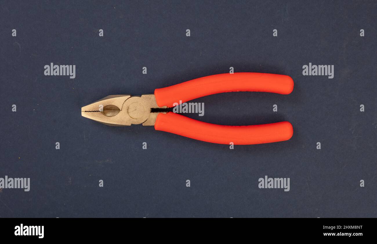 Pliers with steel point, orange color rubber handle on blue background. Hand tool, new metallic clamper, cutter implement for electrician, engineer. O Stock Photo