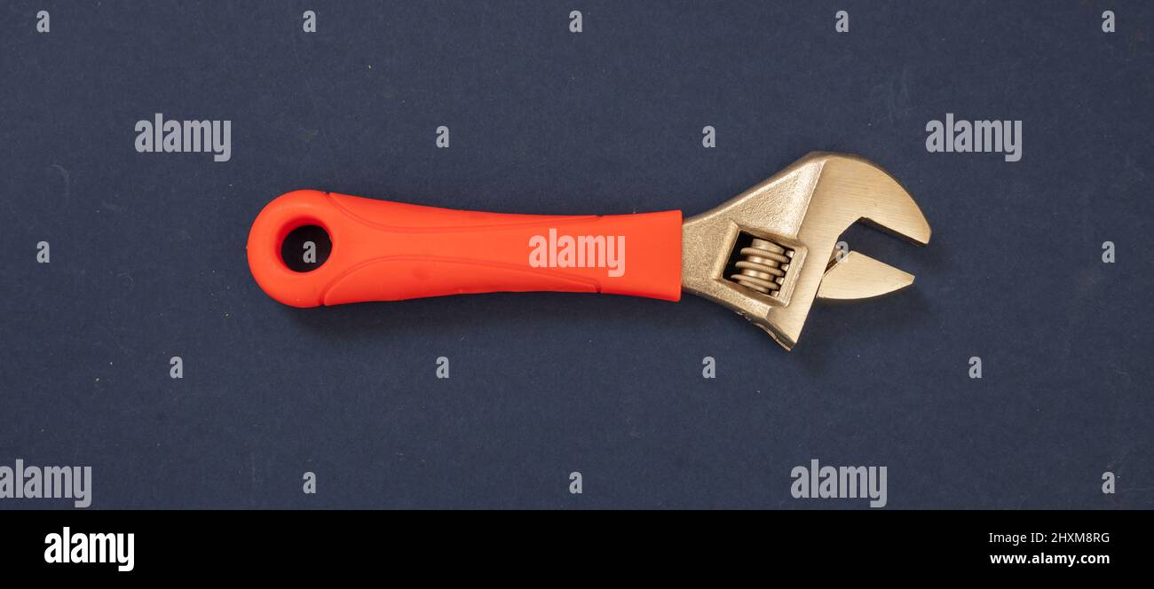 Adjustable wrench with orange color rubber handle on blue background. Hand tool, new metalwork implement for mechanical, locksmith, plumber. Stock Photo