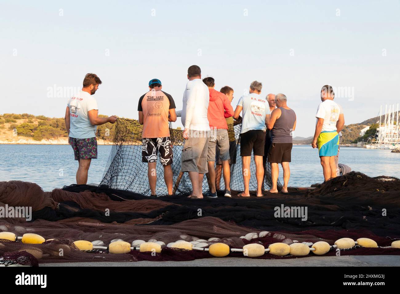 Tribunj, Croatia- August 23, 2021: Group of fishermen repairing the fishing net on the seaside dock Stock Photo